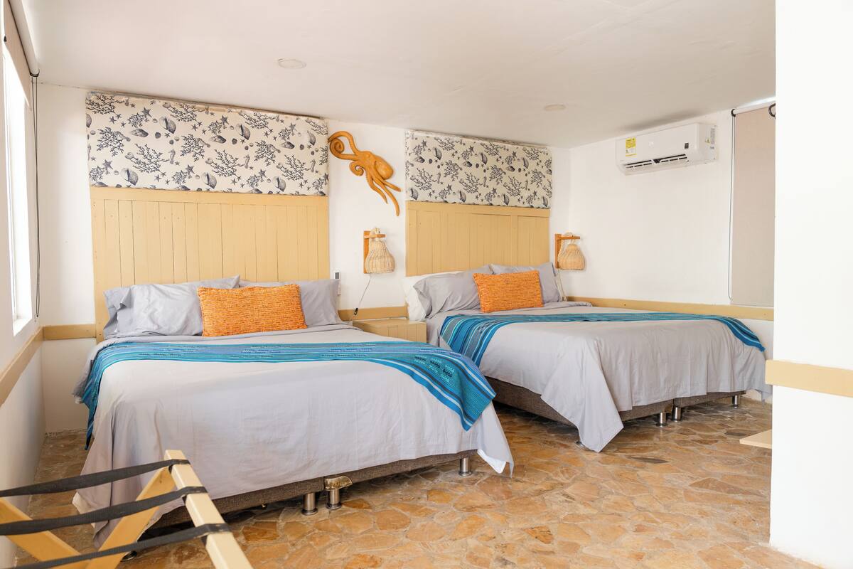 Una habitación con dos camas, cabecero de madera, suelo de piedra y aire acondicionado instalado en la pared.