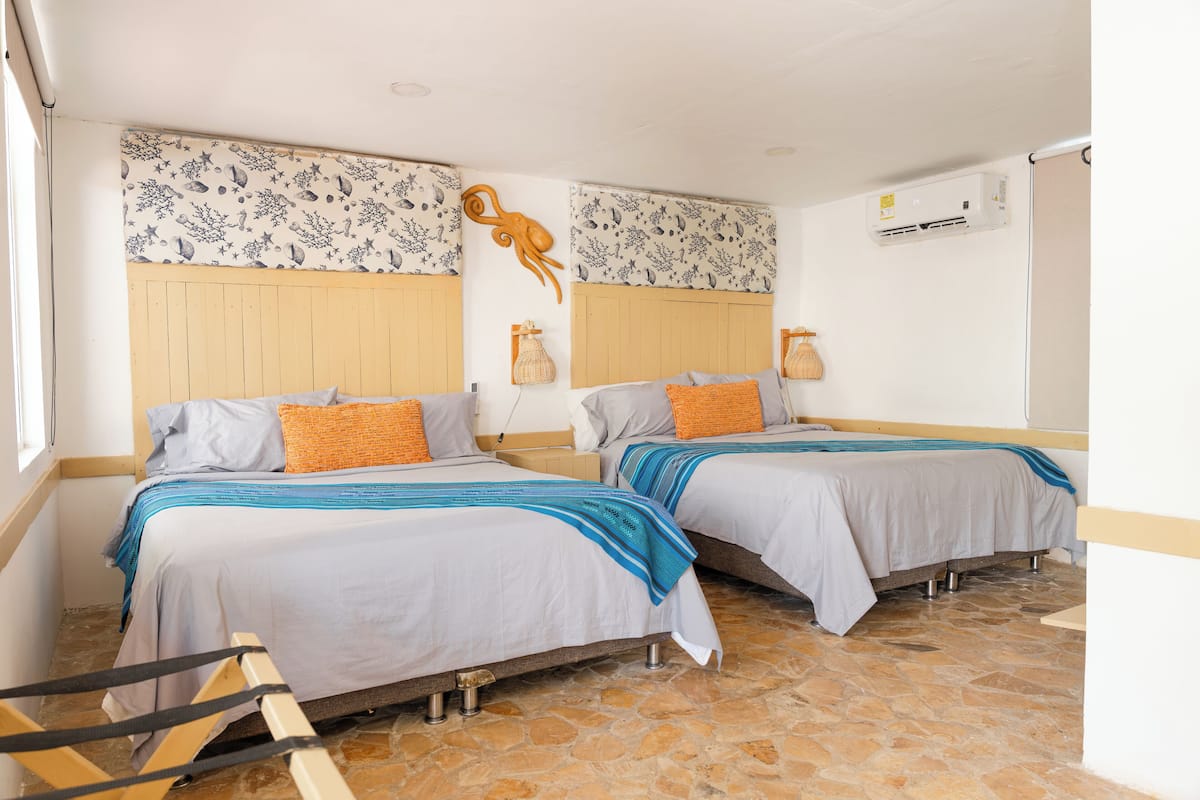 Una habitación con dos camas, cabecero de madera, suelo de piedra y aire acondicionado instalado en la pared.