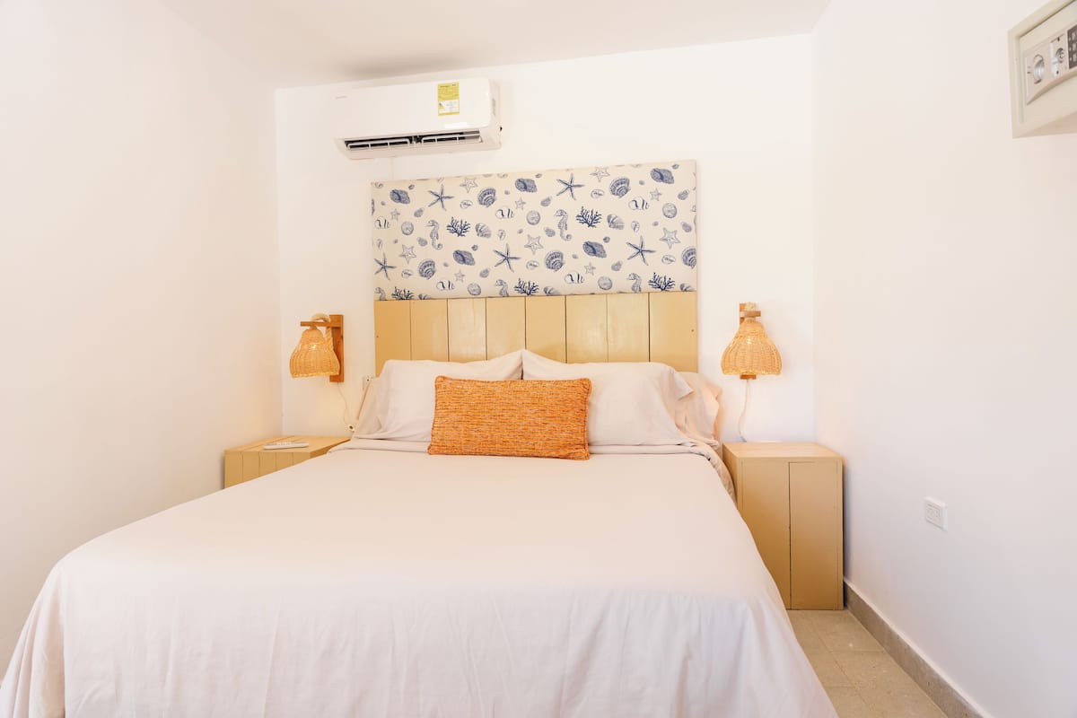 Una cama con sábana blanca, cabecera de madera y pared decorada.