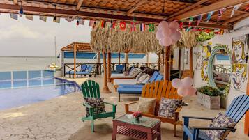 A beachside lounge with a pool, lounge chairs, and a view of the ocean. Flags and balloons are visible.
