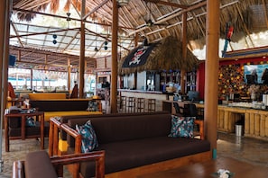 A restaurant with wooden furniture, a bar area, and a thatched roof. - Hotel Isla Real (Cartagena)