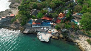 An aerial view of a coastal property with a swimming pool, thatched-roof buildings, and a dock extending into the water. - Hotel Isla Real (Cartagena)