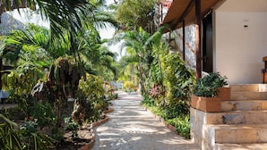 A stone pathway flanked by lush greenery and a building with a white exterior and dark doors. - Hotel Isla Real (Cartagena)