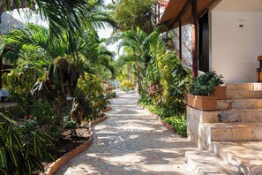 A stone pathway flanked by lush greenery and a building with a white exterior and dark doors. - Hotel Isla Real (Cartagena)