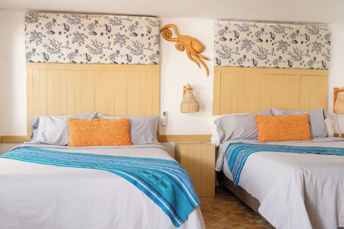 A hotel room with two beds, each with a patterned headboard, a decorative wall piece, and a small bedside table.