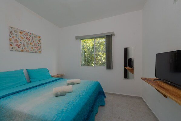 A bedroom with a bed, a TV, a window, and a painting on the wall.