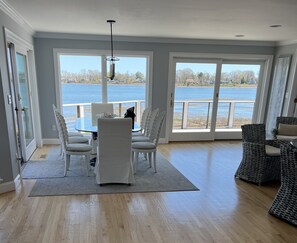 Un comedor con mesa y sillas, ventanas amplias con vista a un lago y un balcón con mobiliario de mimbre.