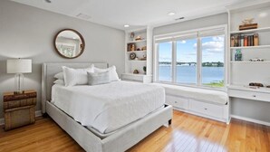Una camera da letto con un letto grande, una finestra vista mare, una libreria e un comodino con una lampada.