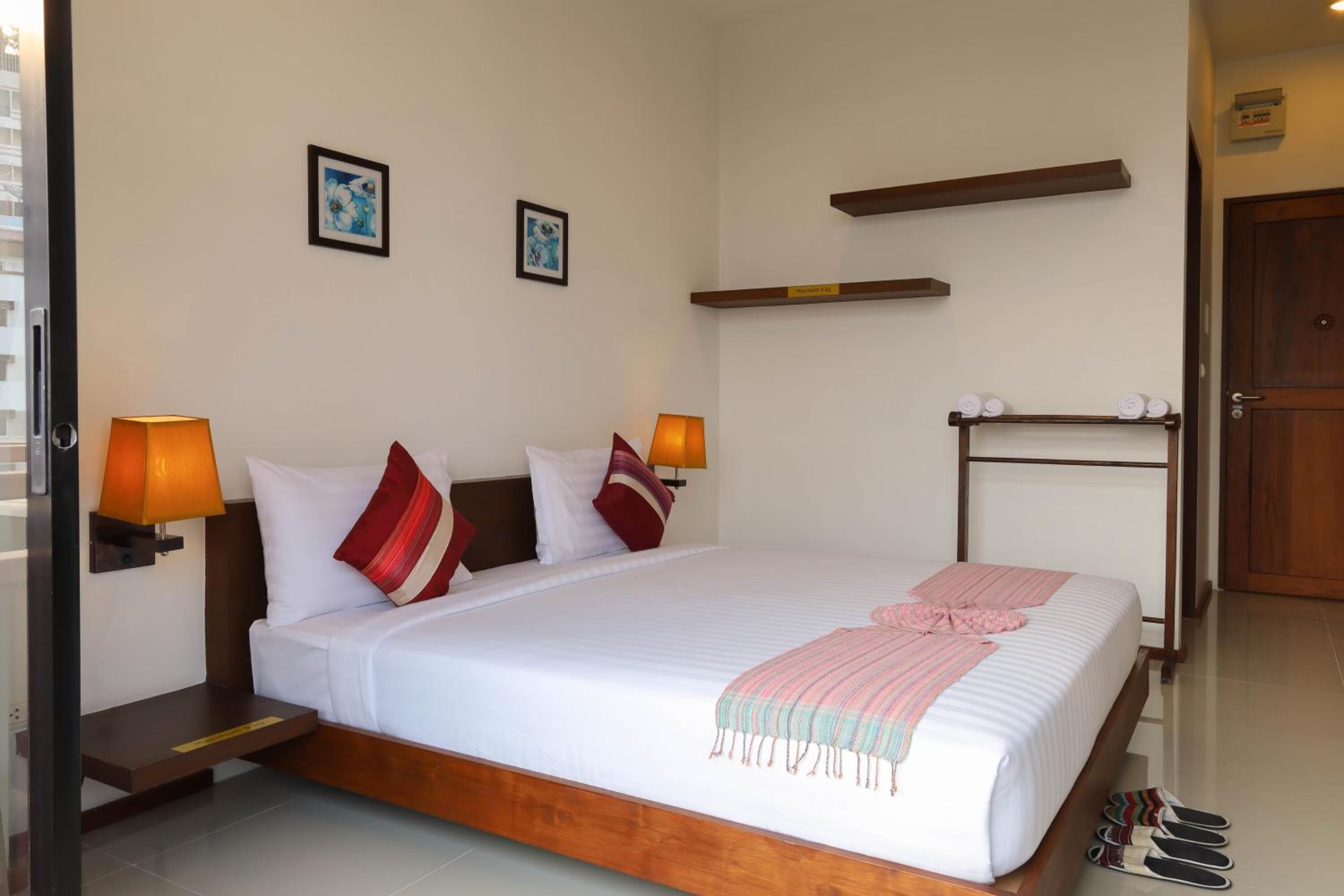 A neatly made bed with white linens and a pink throw, two wall-mounted lamps, and a wooden headboard.