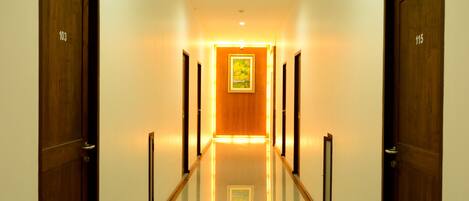A hotel hallway with wooden doors numbered 103 and 115, a polished floor, and a warm light at the end.