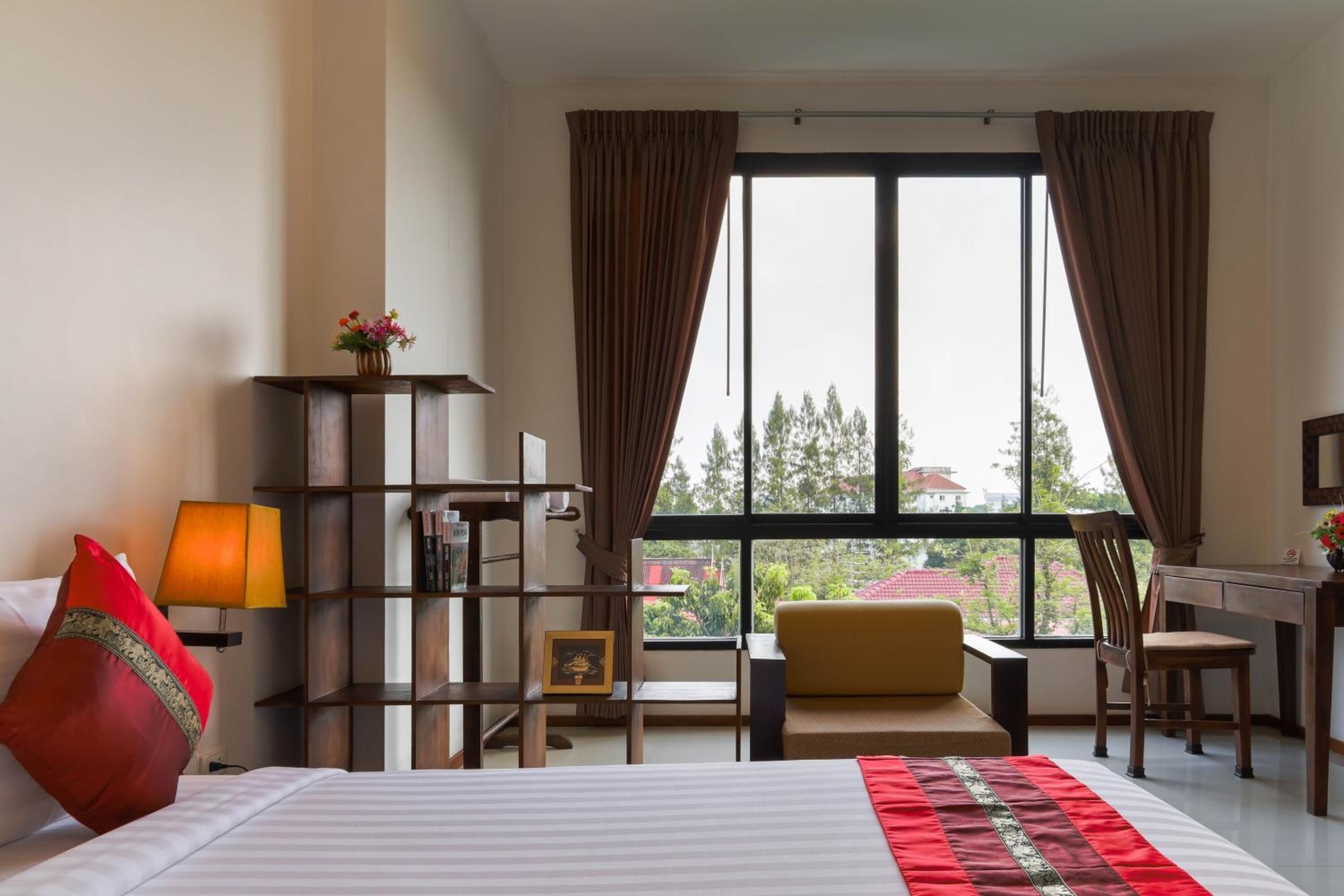 A hotel room with a bed, a desk, a chair, a bookshelf, and a window with curtains.