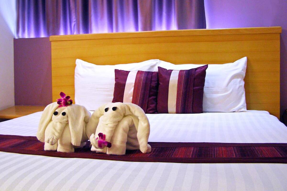 A hotel room with a large bed, a wooden headboard, and two plush toys on the bed.