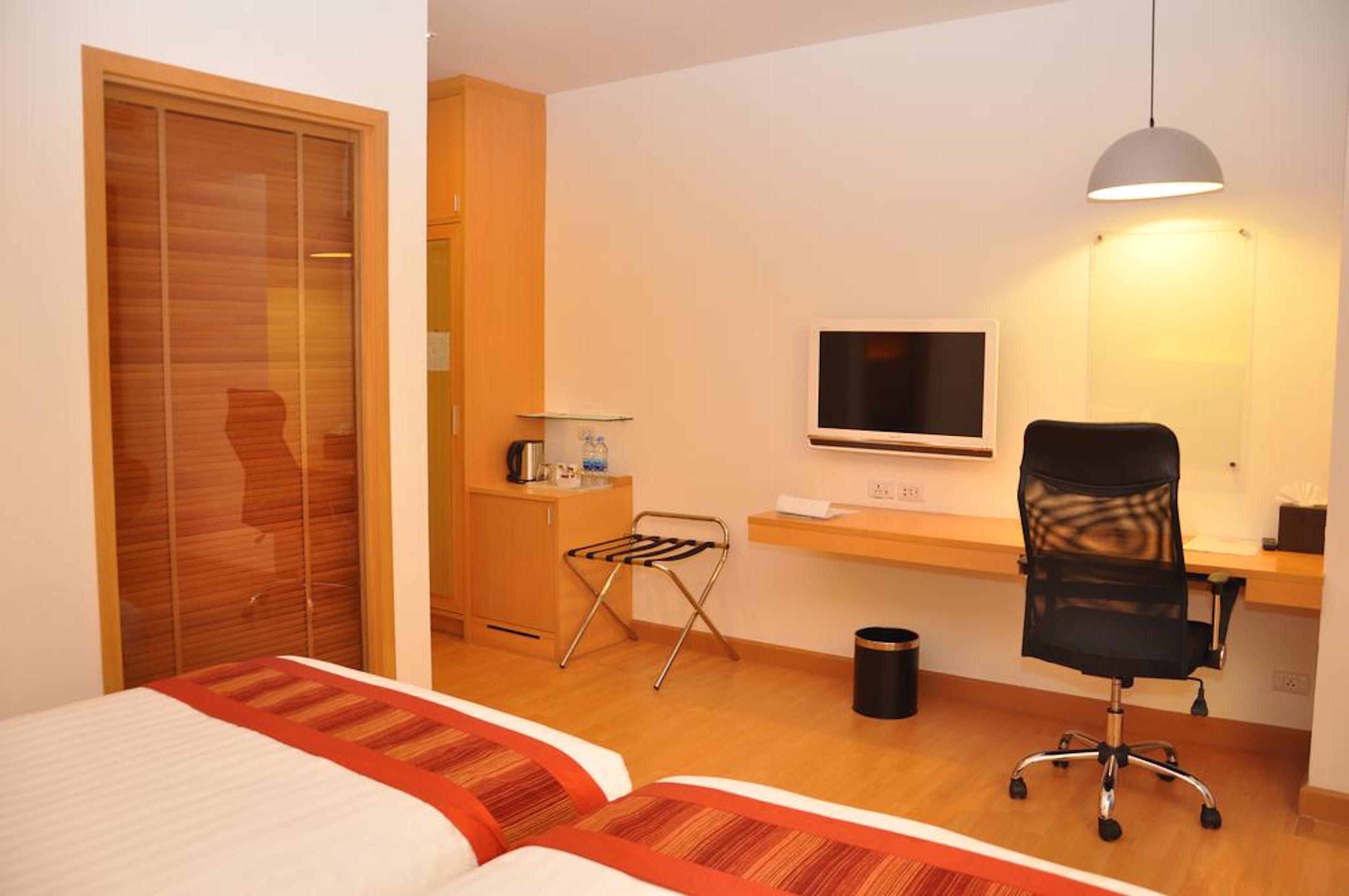Habitación de hotel con dos camas, un escritorio con computadora, un televisor, una silla y una mesita con lámpara.