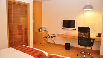 Habitación de hotel con dos camas, un escritorio con computadora, un televisor, una silla y una mesita con lámpara.