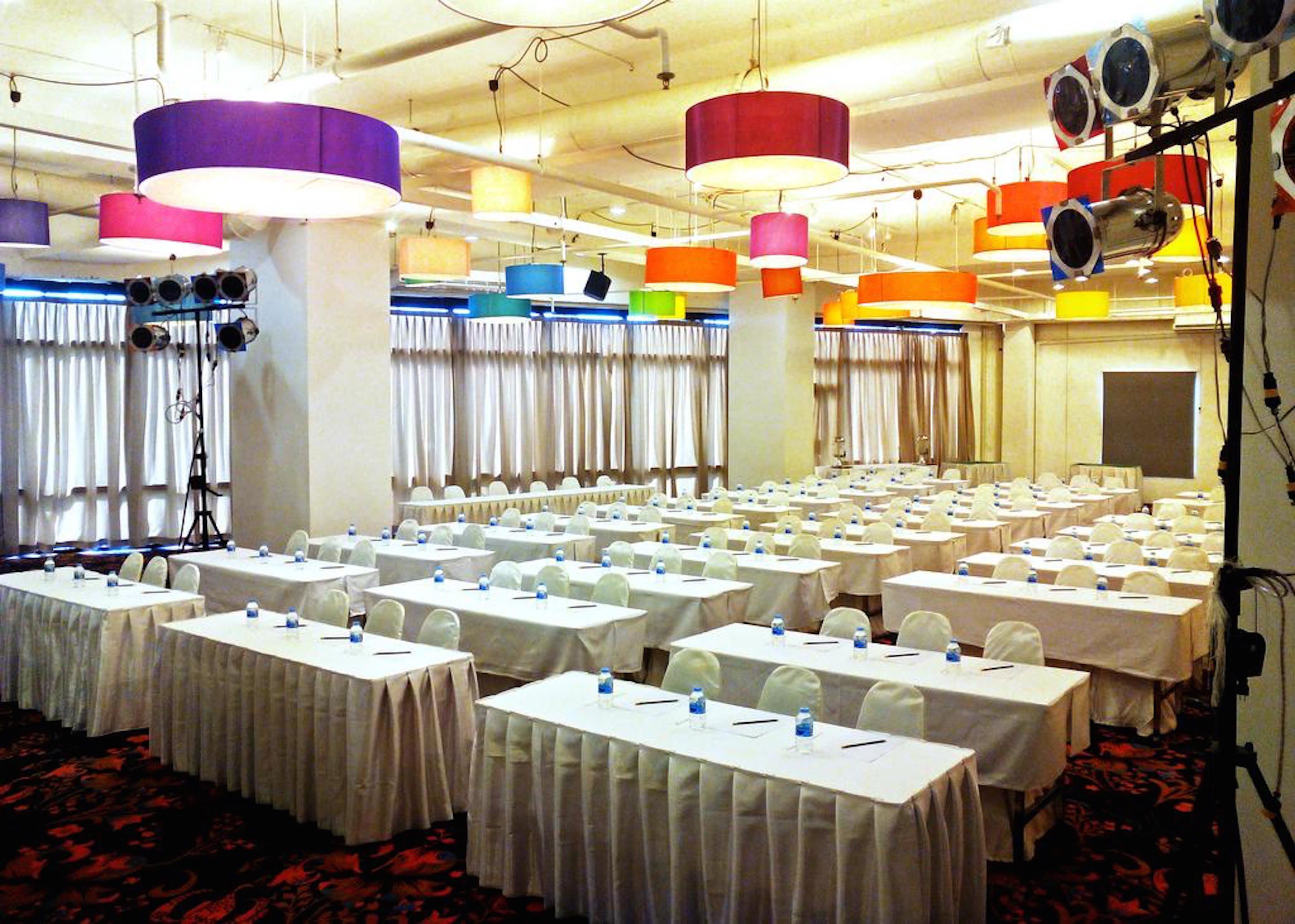 A conference room with multiple tables, white tablecloths, and colorful hanging lamps.