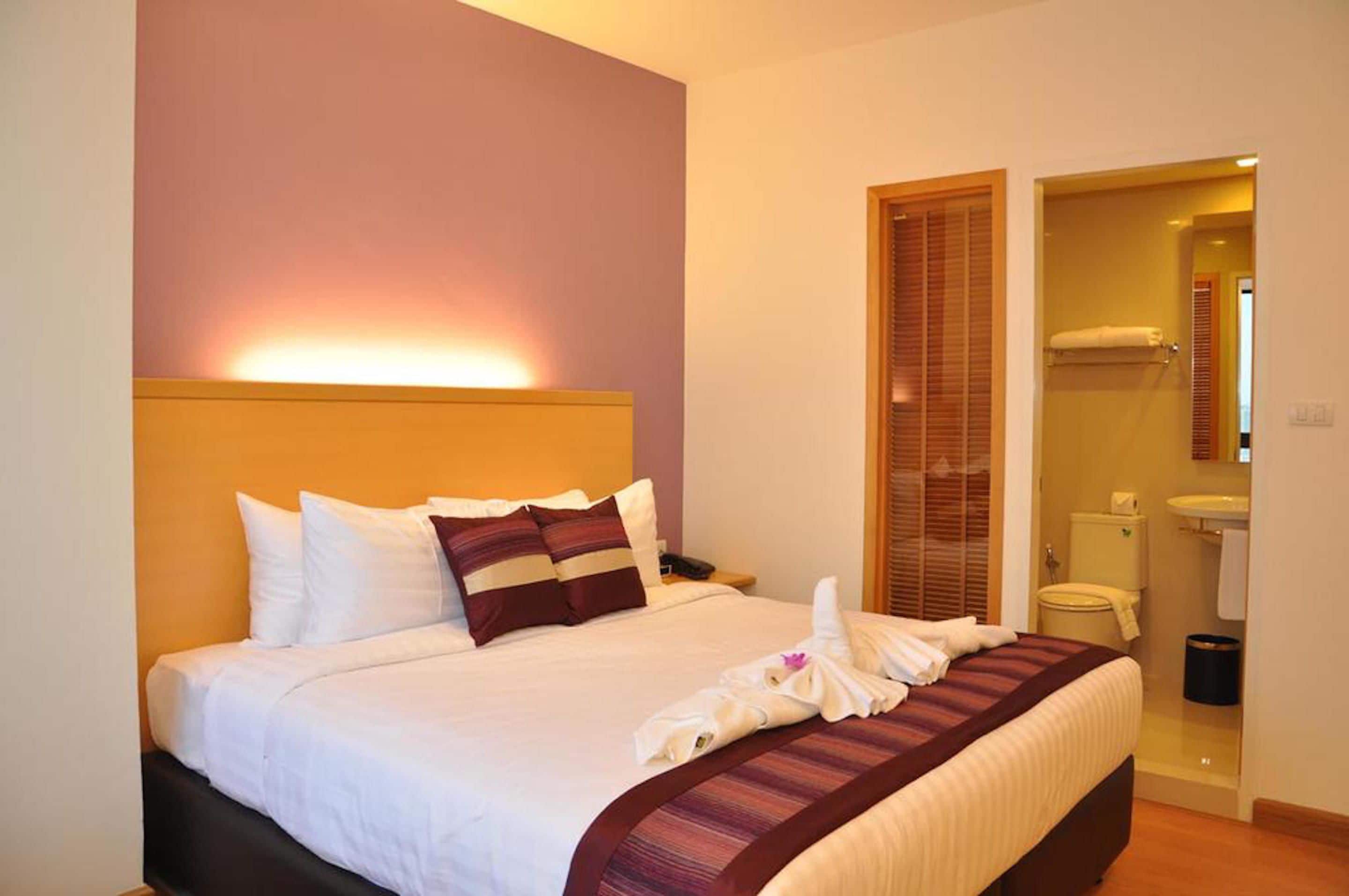 A hotel room with a bed, a nightstand, a bedside table, a bathroom with a toilet and sink, and a shower area.