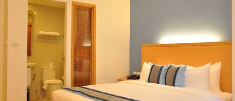A hotel room with a bed, a nightstand, a bathroom with a toilet and sink, and a wooden door.
