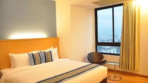 Habitación de hotel con una cama grande, una silla, una mesita y una ventana con vistas a la ciudad.