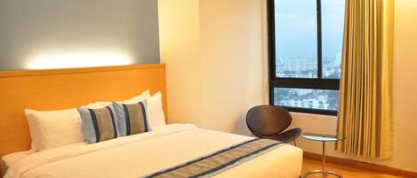 Habitación de hotel con una cama grande, una silla, una mesita y una ventana con vistas a la ciudad.