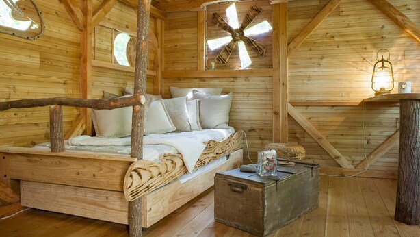 Ein rustikales Holzhaus-Interieur mit einem Bett, einer Holzkommode und einem Ventilator.