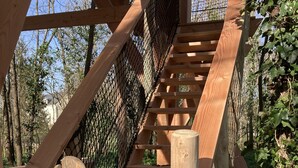 Eine Holztreppe mit einem Metallgitter am Eingang, umgeben von Grünpflanzen.