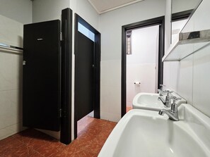 A bathroom with two sinks, a shower, and a door leading to another room. - Panania Hotel (Panania)
