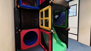A play structure with multiple slides and climbing areas, including a yellow slide and a red climbing wall.