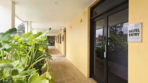 A motel corridor with a 'Motel Entry' sign, potted plants, and a tiled floor.