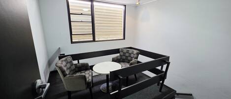 Um quarto pequeno com sofá, mesa redonda e janela com persianas.