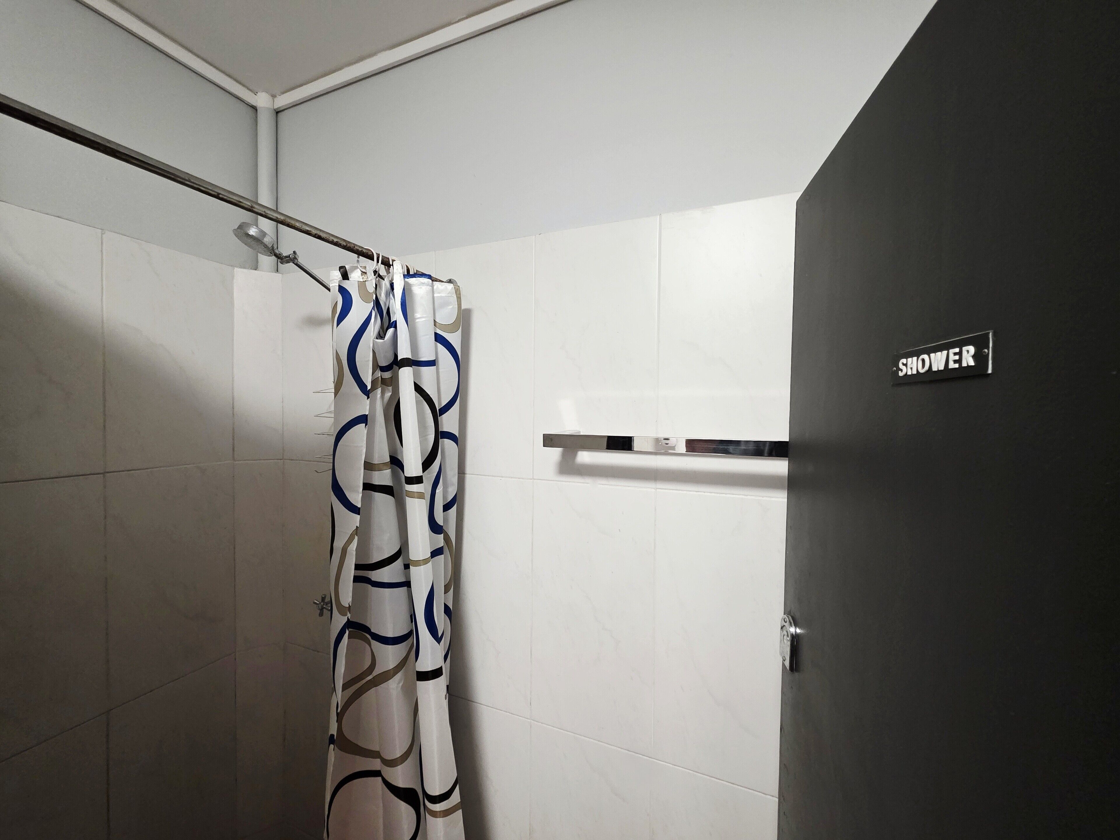A shower area with a curtain, a towel rack, and a sign indicating the shower location.