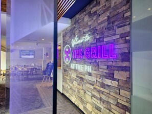 A restaurant interior with a stone wall and neon sign reading "Welcome to THE GRILL AT THE PH". - Panania Hotel (Panania)