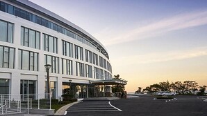 A modern building with a curved facade, large windows, and a parking lot. - Potalaka Naksan Beach Wellness (Yangyang)