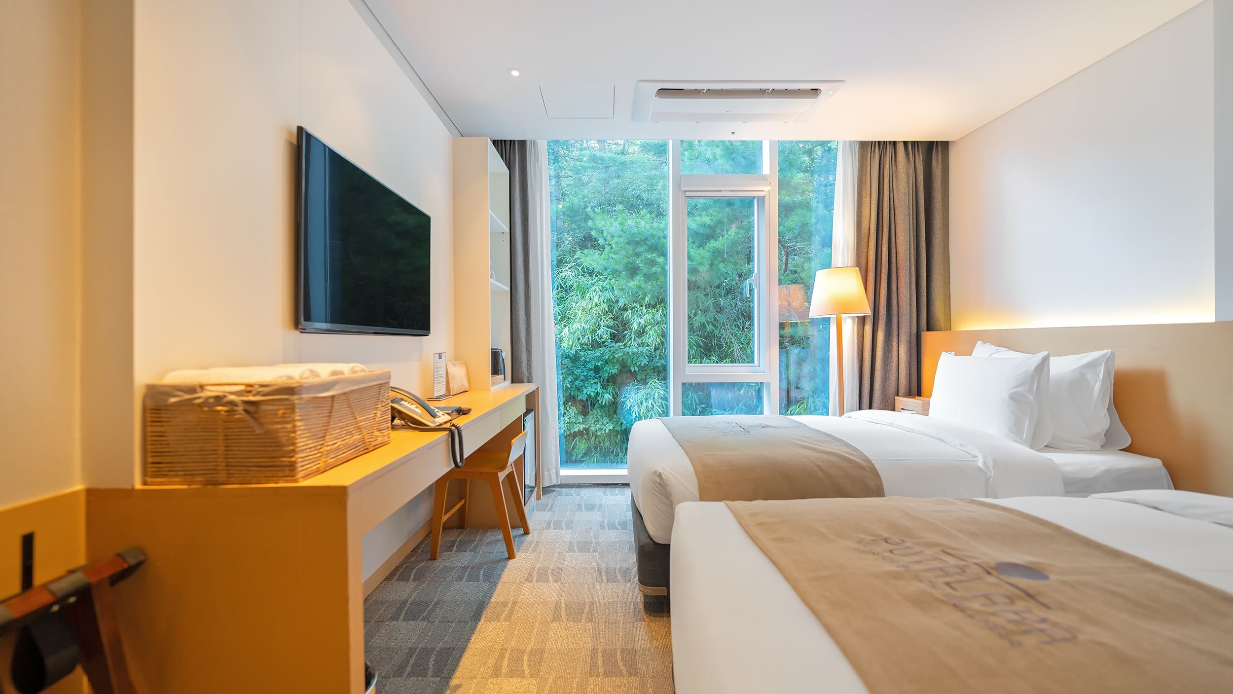 Habitación de hotel con escritorio, dos camas, televisor y vistas a zonas verdes.