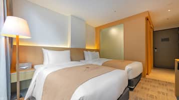 Habitación de hotel con dos camas, una mesita de noche, una lámpara y una puerta.