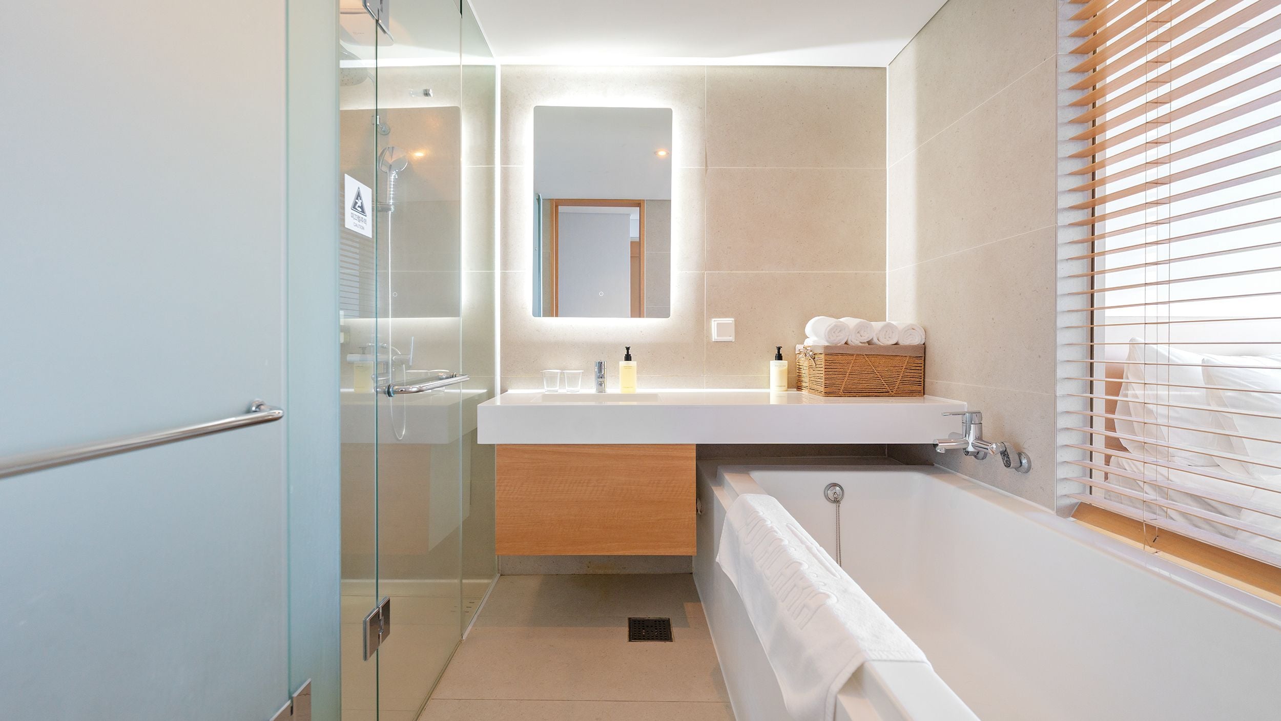 Un bagno moderno con cabina doccia in vetro, mobile lavabo in legno, vasca da bagno e finestra con persiane.