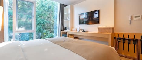 Habitación de hotel con una cama grande, un escritorio con computadora, televisión y vistas a zonas verdes.