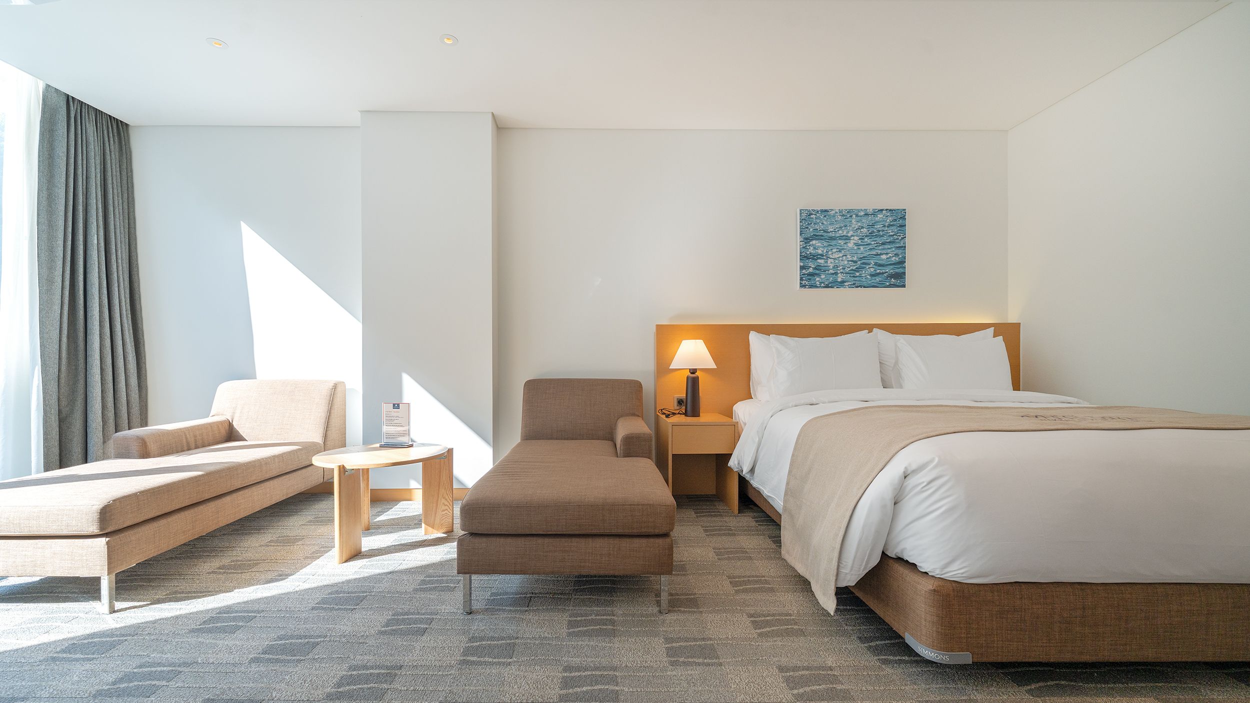Una habitación de hotel con cama, sofá, sillón, mesita de noche y lámpara.