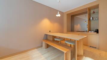 A modern kitchen with a wooden table and bench, a hanging light fixture, and a mirrored backsplash.