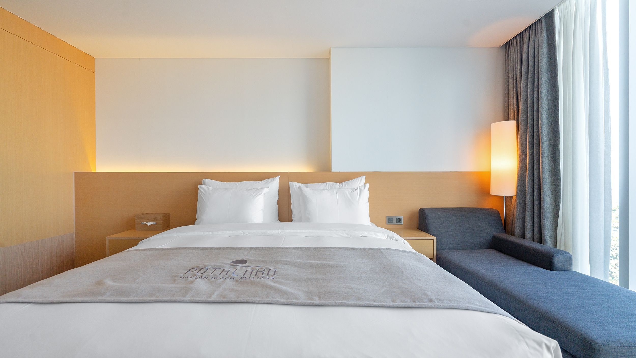 Una habitación de hotel con una cama grande, una mesita de noche, una silla y un televisor montado en la pared.