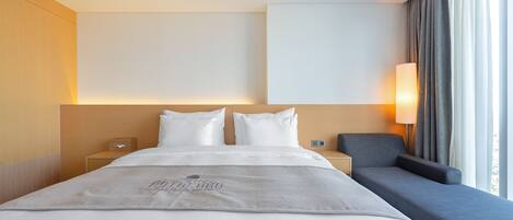 Una habitación de hotel con una cama grande, una mesita de noche, una silla y un televisor montado en la pared.