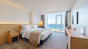 Une chambre d’hôtel équipée d’un lit, d’une table de chevet, d’un bureau et d’une grande fenêtre donnant sur la mer.