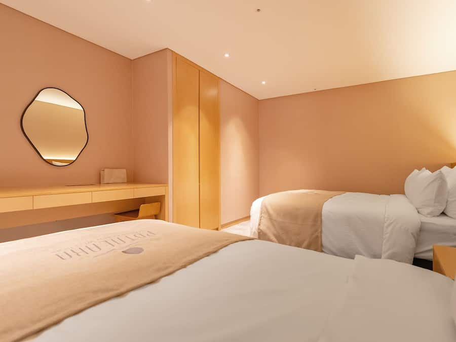 Una habitación de hotel con una cama, una mesita de noche, un espejo y un armario.