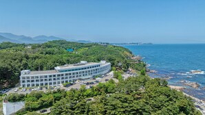 A modern building with a curved facade, surrounded by lush greenery and a coastal view. - Potalaka Naksan Beach Wellness (Yangyang)