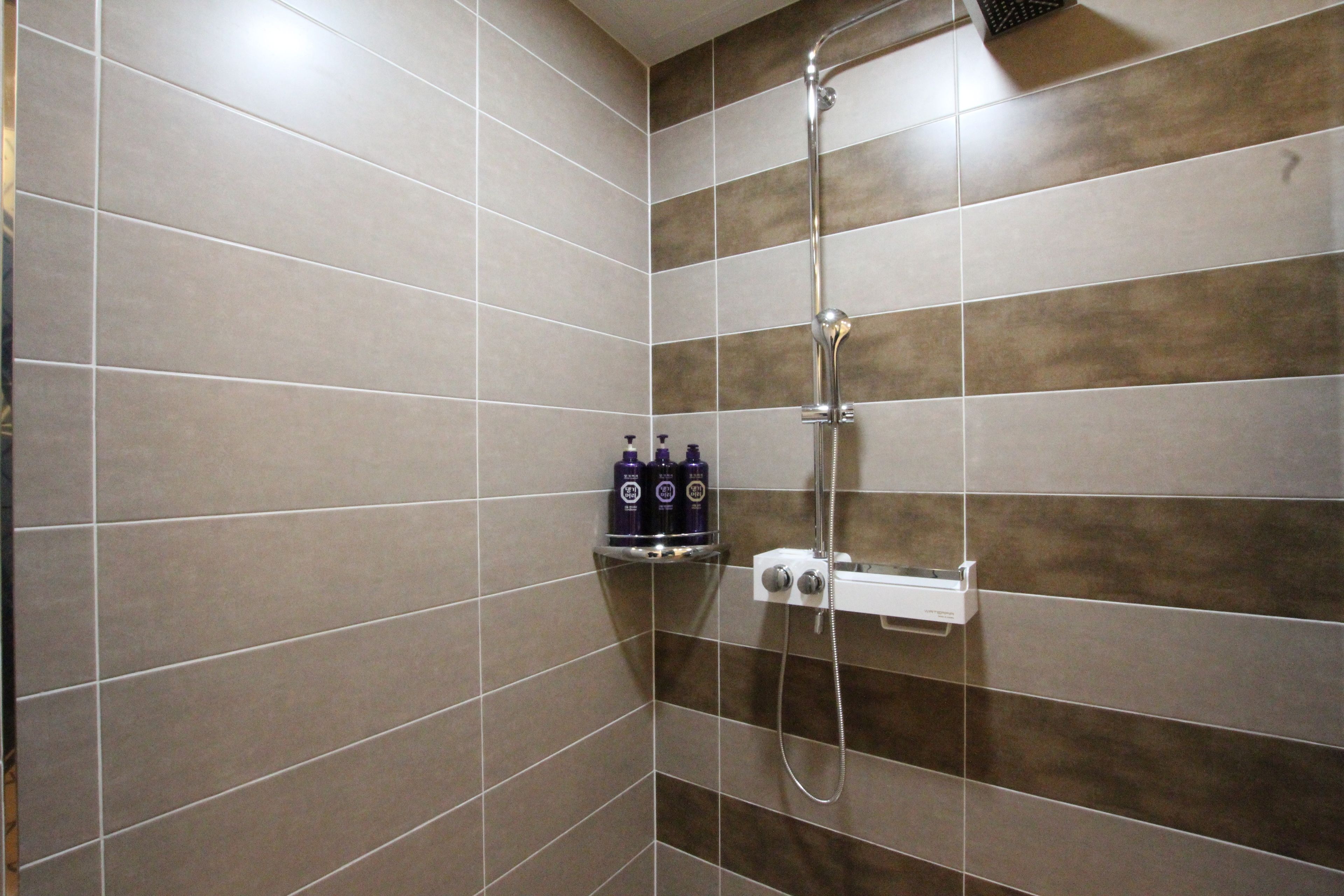 A bathroom with a shower, tiled walls, and two bottles of shampoo on a shelf.