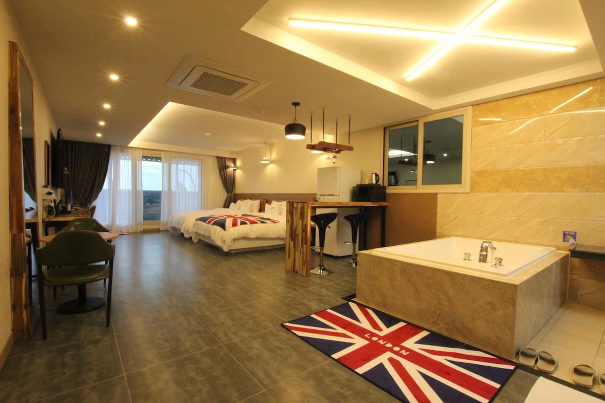 Quarto de hotel moderno com uma cama grande, área de estar, mesa de jantar e banheiro com banheira.