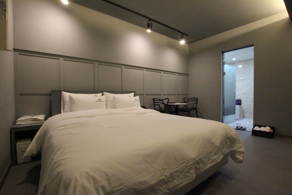 Quarto de hotel moderno com uma cama grande, mesa de cabeceira e pequena escrivaninha com cadeira.