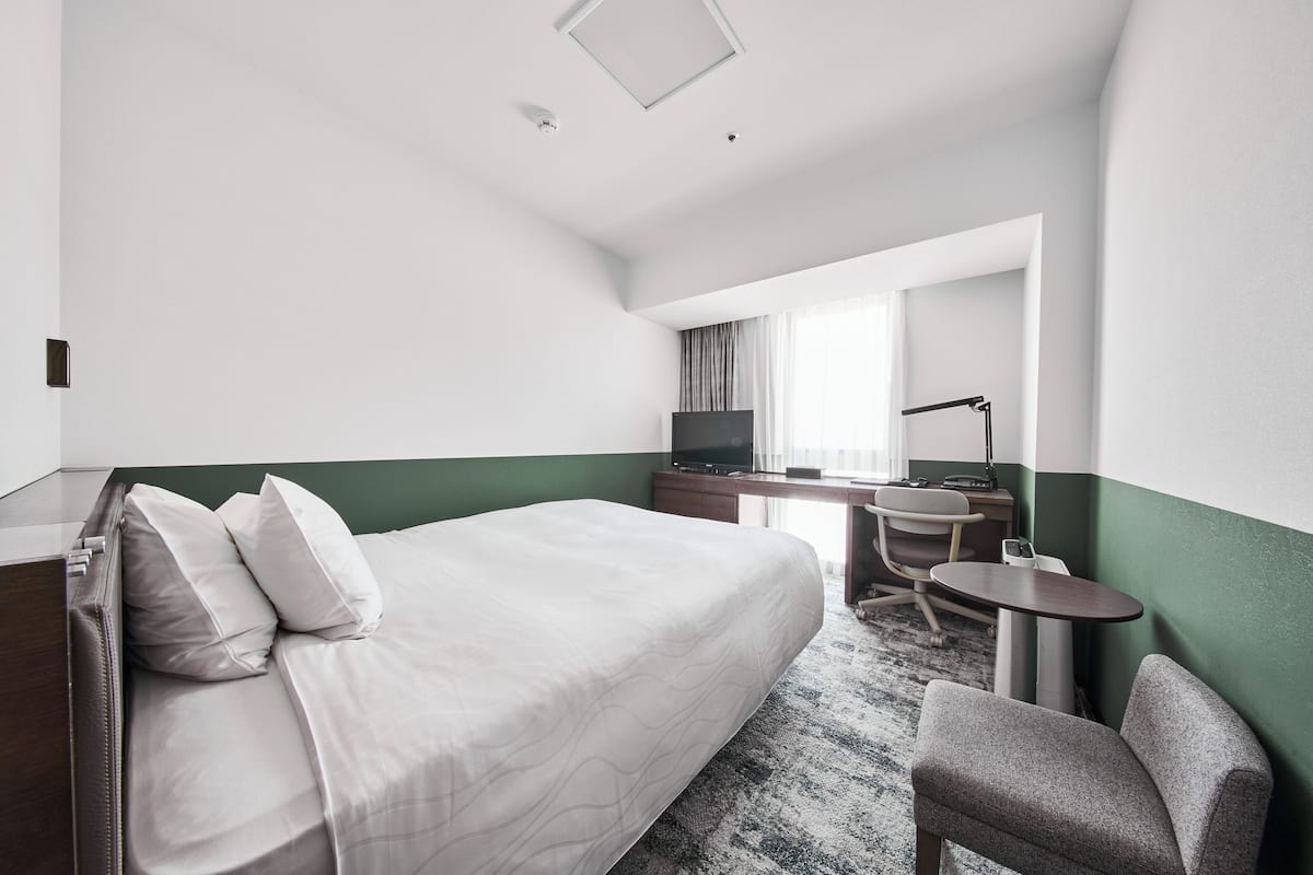 A hotel room with a large bed, a desk, a chair, and a television.