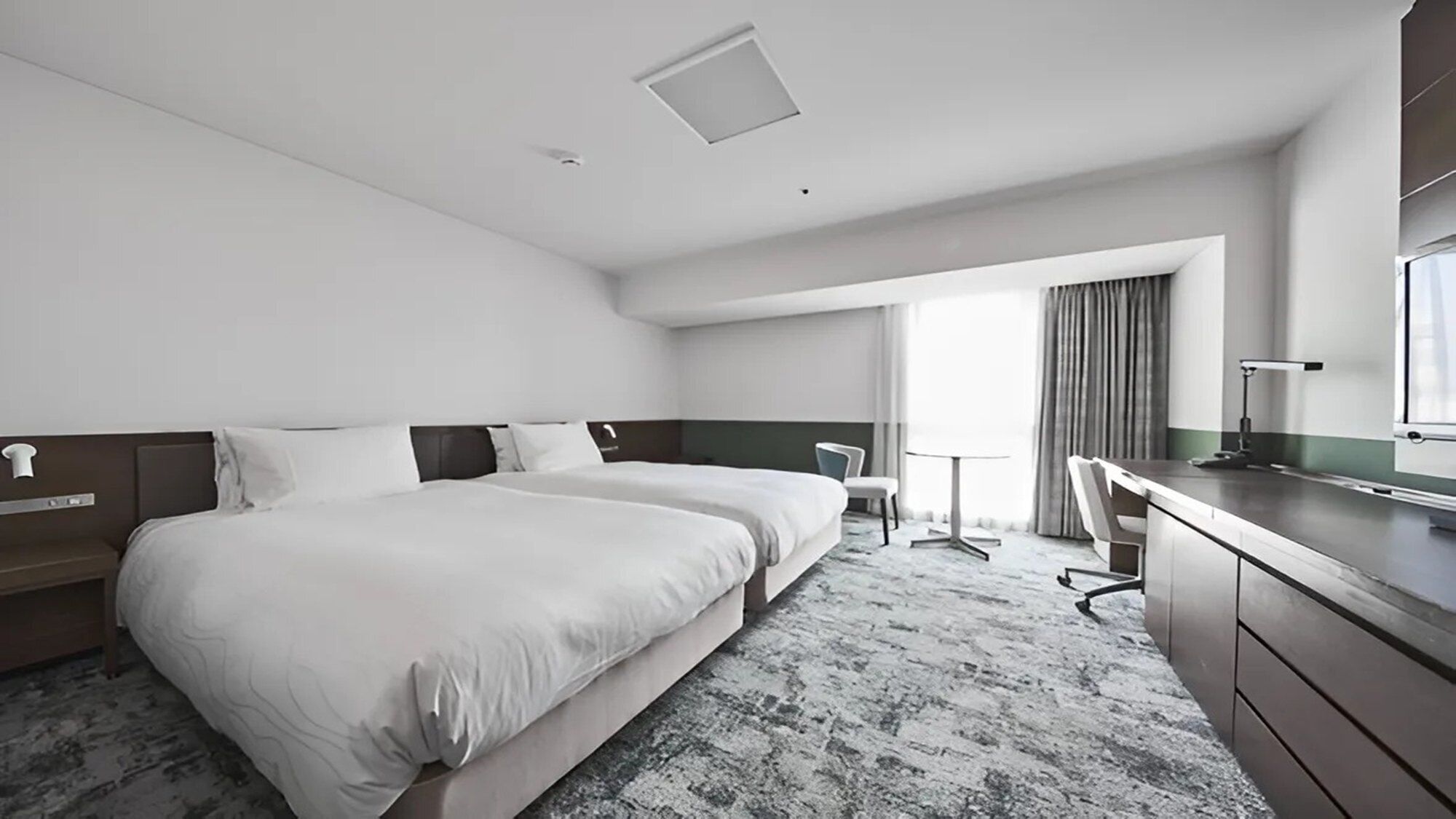 Quarto de hotel com uma cama grande, uma escrivaninha, uma cadeira e uma pequena mesa.