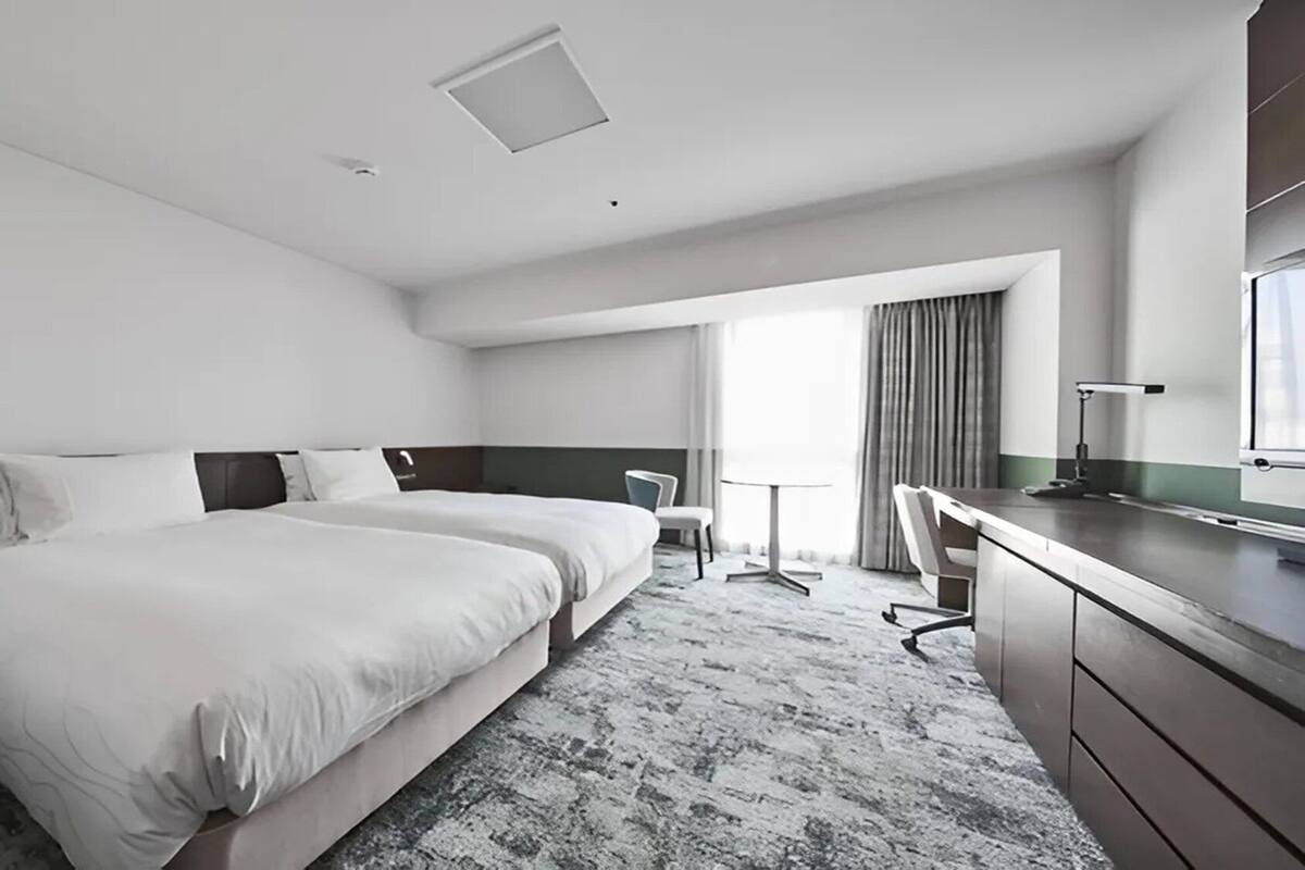 A hotel room with a large bed, a desk, a chair, and a small table.