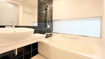 Un baño moderno con un lavamanos blanco, paredes cubiertas de azulejos negros, un espejo grande y una bañera.